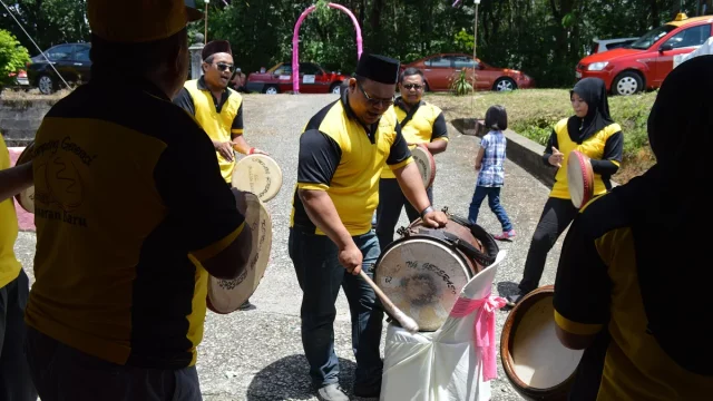 Beberapa laki-laki berseragam kuning hitam memukul kompang dan sebuah bass drum di jalan