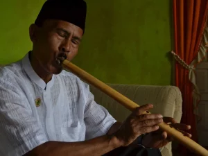 Seorang pemain meniup saluang darek sambil duduk di ruang tamu