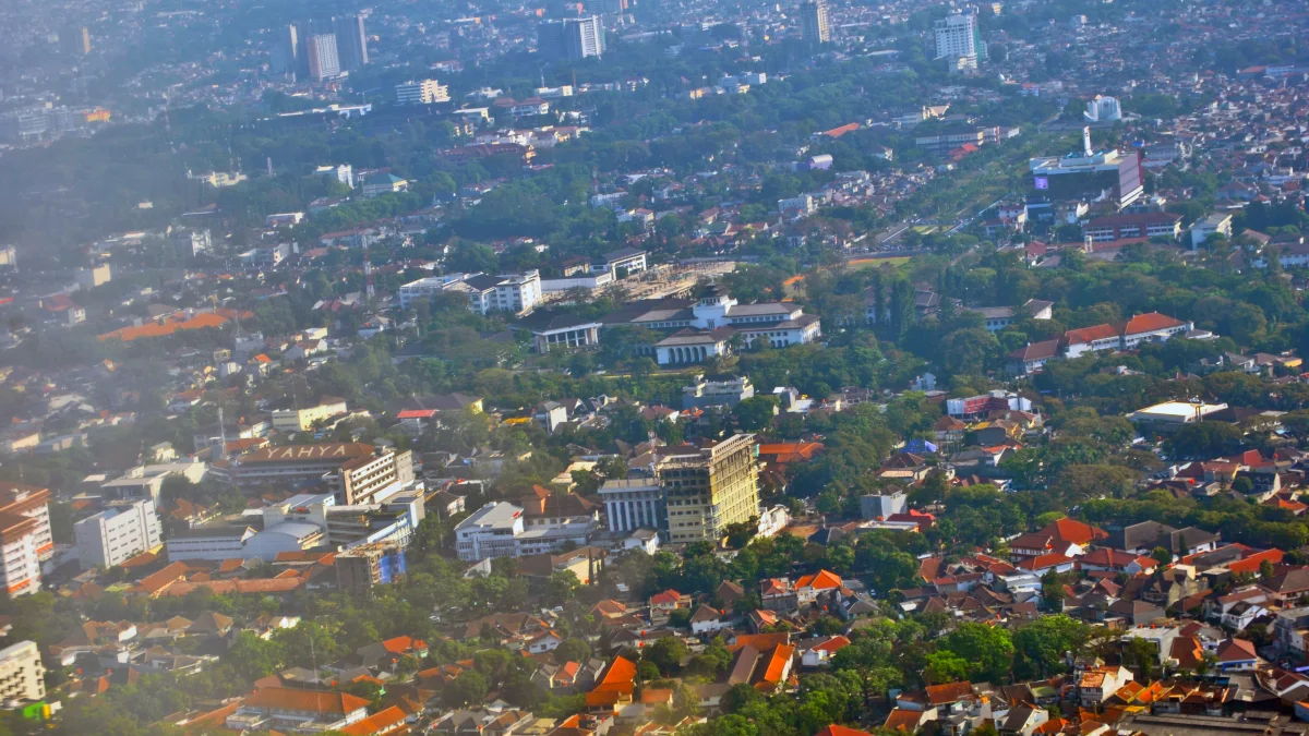 Pemandangan udara permukiman padat dan gedung bertingkat di antara pepohonan Kota Bandung
