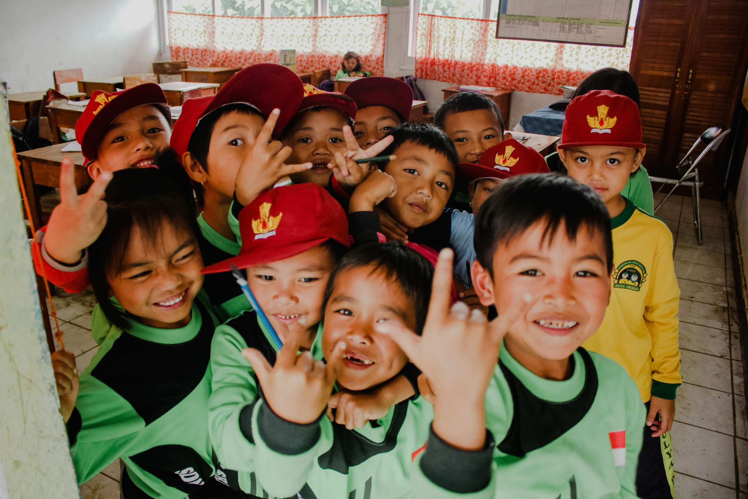 Tujuh Anak Tertinggal Ketukan di Kelas Tari Pekanbaru 2 Ilustrasi murid-murid sekolah berseragam hijau di dalam kelas melambaikan tangan.