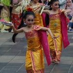 Ilustrasi sejumlah penari muda berbusana tradisi warna emas dan merah menampilkan tarian.