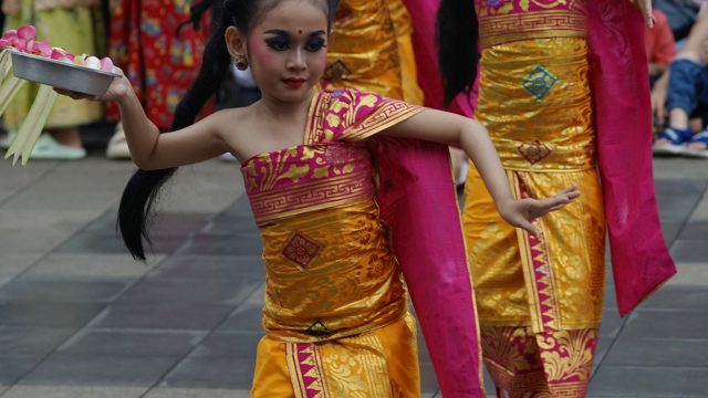 Ilustrasi sejumlah penari muda berbusana tradisi warna emas dan merah menampilkan tarian.