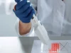 Tangan peneliti bersarung tangan menggunakan pipet di atas wadah sampel di laboratorium