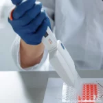 Tangan peneliti bersarung tangan menggunakan pipet di atas wadah sampel di laboratorium