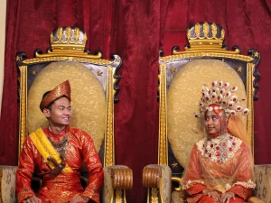 Sepasang pengantin mengenakan pakaian adat Melayu Deli lengkap dengan tutup kepala