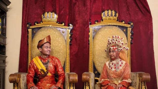 Sepasang pengantin mengenakan pakaian adat Melayu Deli lengkap dengan tutup kepala