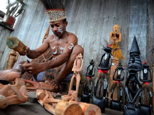 Pengukir kayu Asmat sedang memahat patung kayu tradisional