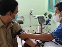 Petugas kesehatan bermasker mengukur tekanan darah pasien dengan tensimeter di ruang klinik, Indonesia