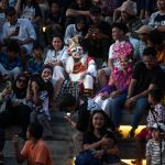 Ilustrasi penonton duduk berdesakan menyaksikan pertunjukan di ruang terbuka.