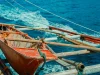 Perahu kayu bercadik berwarna merah melaju di atas laut biru