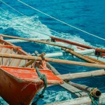 Perahu kayu bercadik berwarna merah melaju di atas laut biru