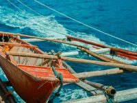Perahu kayu bercadik berwarna merah melaju di atas laut biru