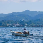 Perahu kecil melintasi perairan Sulawesi Barat dengan perbukitan di kejauhan