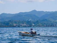 Perahu kecil melintasi perairan Sulawesi Barat dengan perbukitan di kejauhan