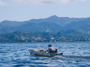 Perahu kecil melintasi perairan Sulawesi Barat dengan perbukitan di kejauhan