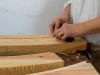 Seorang perajin menghaluskan permukaan papan kayu dengan serutan tangan