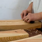Seorang perajin menghaluskan permukaan papan kayu dengan serutan tangan