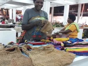Perajin Papua merajut sekaligus menjual noken, tas rajut tradisional Papua.