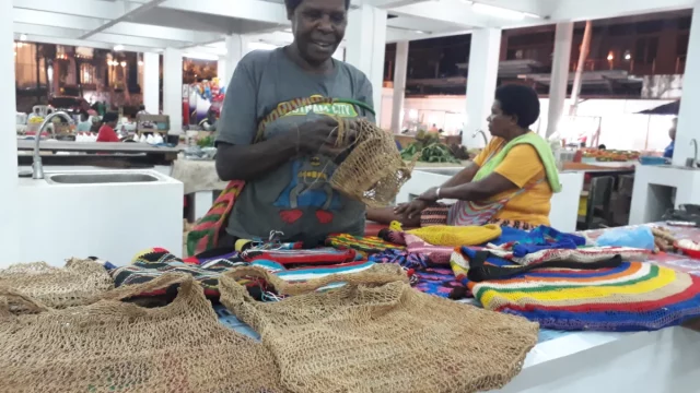 Perajin Papua merajut sekaligus menjual noken, tas rajut tradisional Papua.