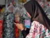 Perempuan berjilbab hitam mengetik di ponsel di depan rak kerupuk toko oleh-oleh