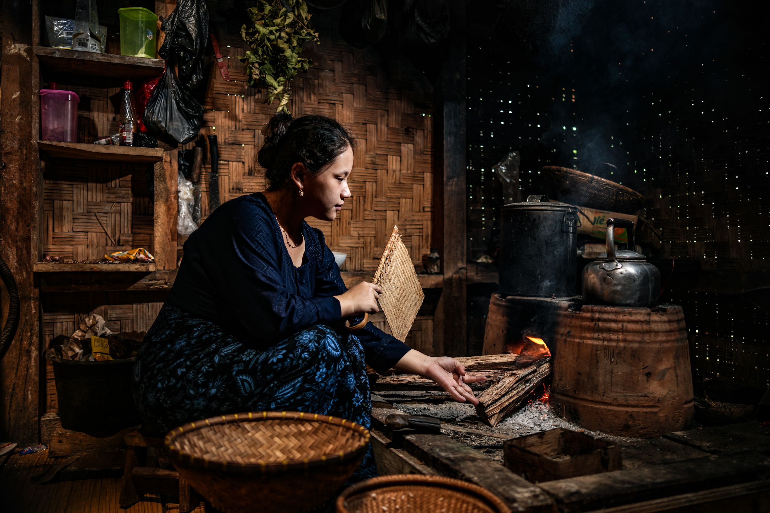 Ilustrasi seorang perempuan menjaga tungku kayu di dapur tradisional.