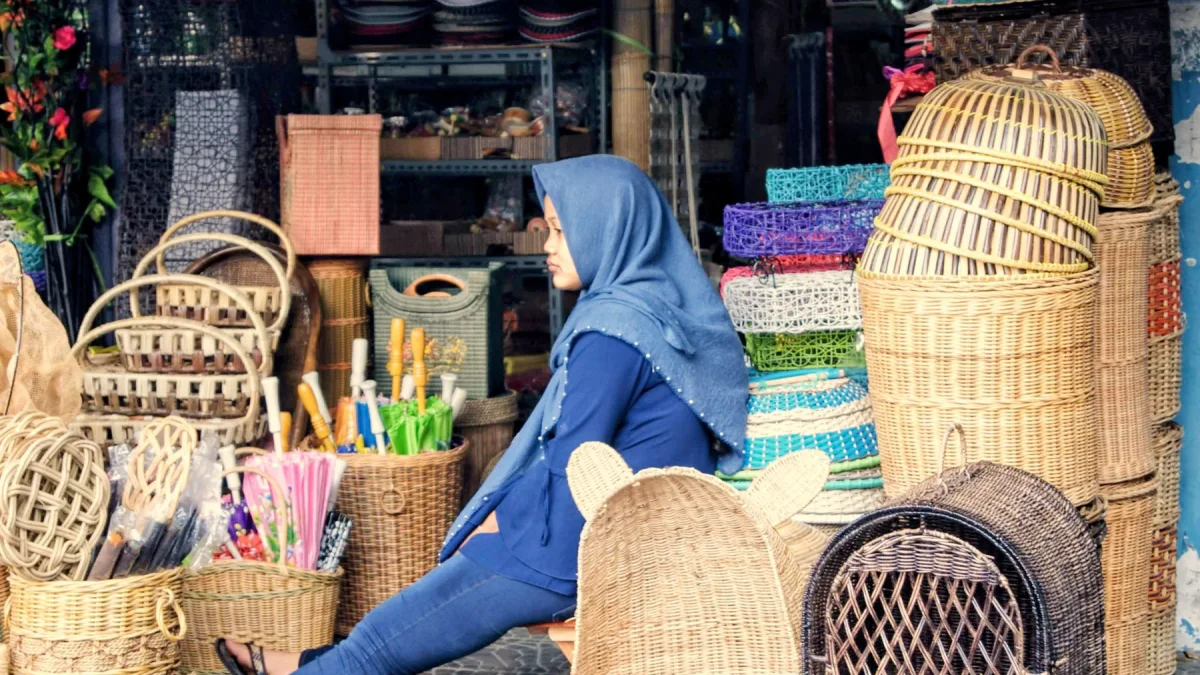 Perempuan berkerudung biru duduk di antara keranjang anyaman di kios pasar