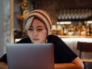 Perempuan berkupluk garis menatap layar laptop di meja sebuah kafe