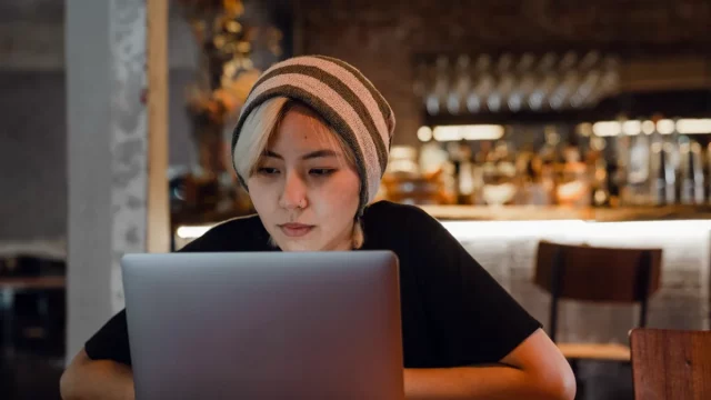Perempuan berkupluk garis menatap layar laptop di meja sebuah kafe