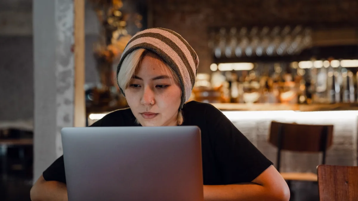 Perempuan berkupluk garis menatap layar laptop di meja sebuah kafe