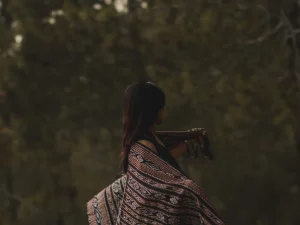 Perempuan berselendang kain tenun Sabu dipotret dari belakang dengan latar pepohonan