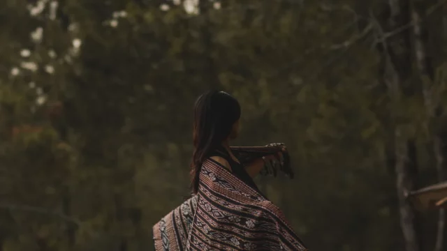 Perempuan berselendang kain tenun Sabu dipotret dari belakang dengan latar pepohonan