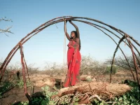 Perempuan Somalia berbaju merah mengikat kerangka kayu rumah tradisional aqal di perdesaan Somalia