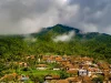 Permukiman desa beratap genting di kaki perbukitan berhutan yang berkabut