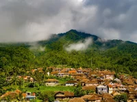 Permukiman desa beratap genting di kaki perbukitan berhutan yang berkabut