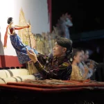 Seorang dalang memainkan wayang di bawah sorot lampu panggung