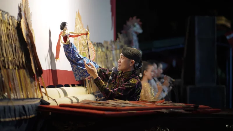 Seorang dalang memainkan wayang di bawah sorot lampu panggung