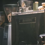 Mesin espreso, penggiling kopi, dan cangkir di meja sebuah kedai kopi