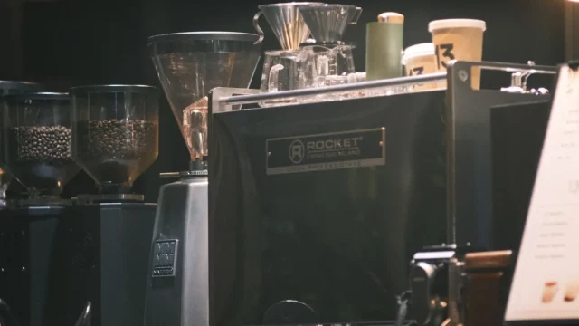 Mesin espreso, penggiling kopi, dan cangkir di meja sebuah kedai kopi