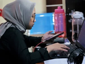 Ilustrasi petugas berkerudung bekerja di meja kantor dengan laptop dan telepon