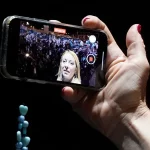Tangan memegang ponsel yang merekam Giorgia Meloni di hadapan massa