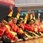 Sekelompok penari Indang berbaju merah dan kuning duduk berbaris sambil mengangkat tangan
