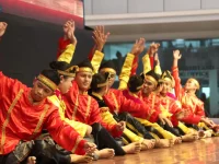 Sekelompok penari Indang berbaju merah dan kuning duduk berbaris sambil mengangkat tangan