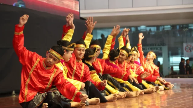 Sekelompok penari Indang berbaju merah dan kuning duduk berbaris sambil mengangkat tangan