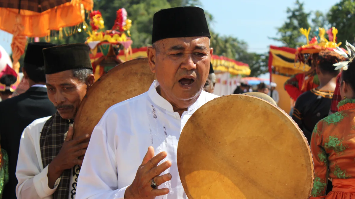 Dua laki-laki berkopiah memukul rebana besar berbingkai kayu pada sebuah arak-arakan
