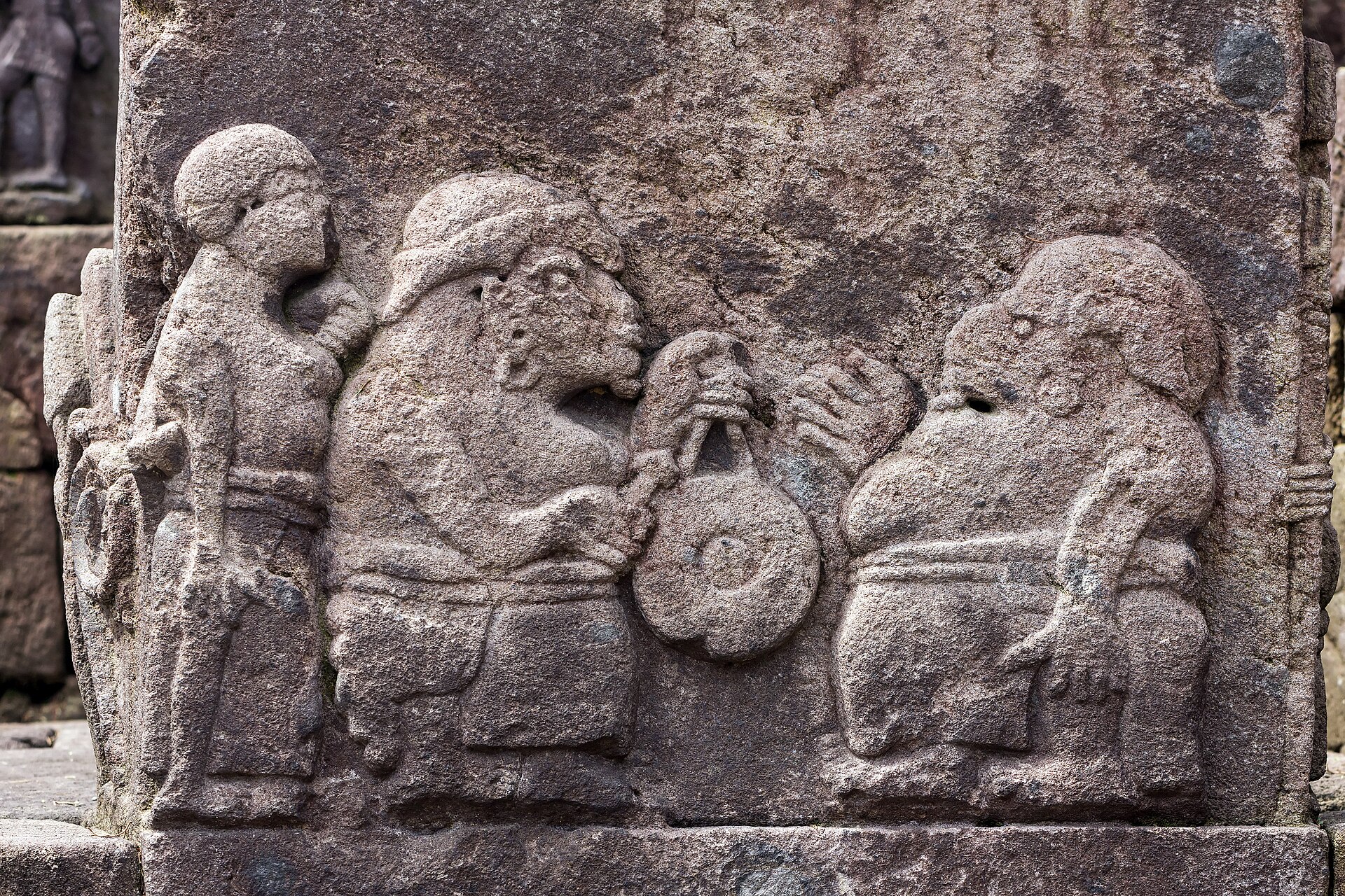 Relief batu di Candi Sukuh yang memahat tiga sosok manusia berdiri berjajar.