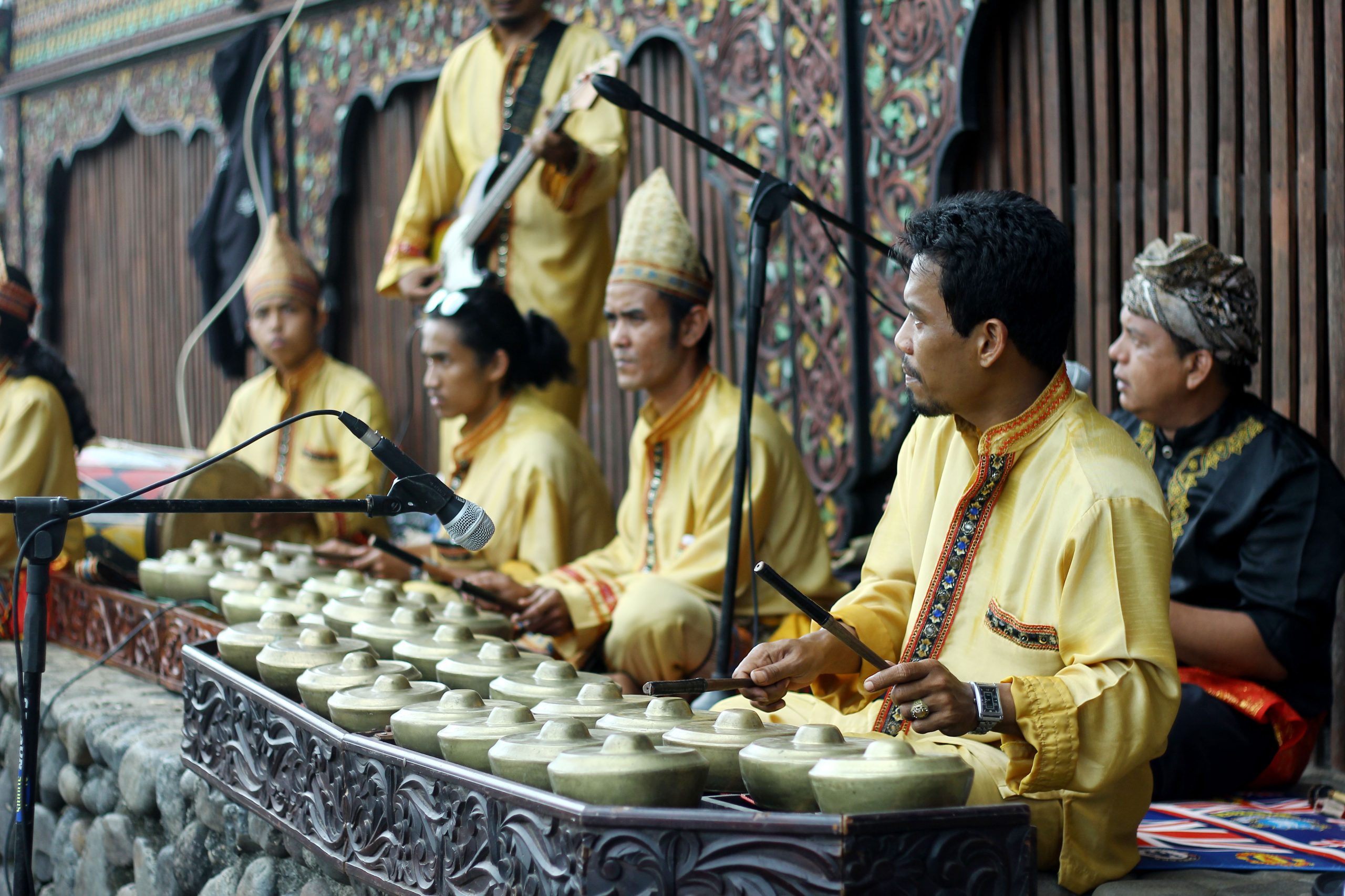 Pemain talempong berbusana kuning memukul deretan gong kecil Minangkabau.