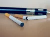 Rokok elektrik berbentuk pena tergeletak di meja di belakang dua batang rokok biasa