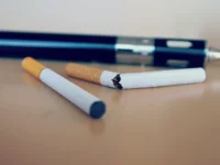 Rokok elektrik berbentuk pena tergeletak di meja di belakang dua batang rokok biasa