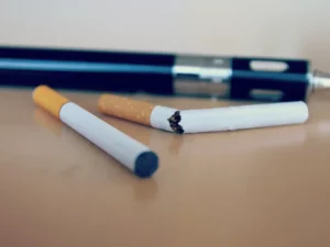 Rokok elektrik berbentuk pena tergeletak di meja di belakang dua batang rokok biasa
