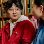Dua orang membaca di antara rak buku perpustakaan